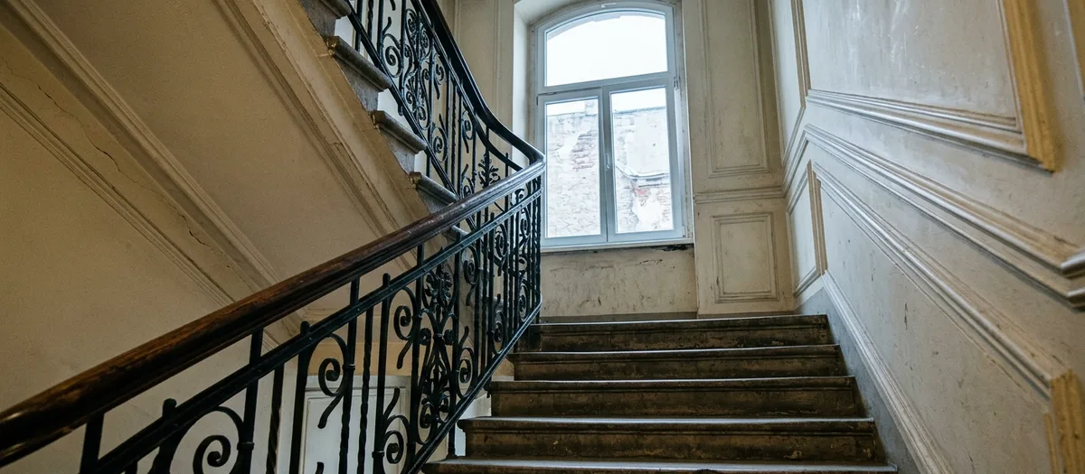 Blick das Gründerzeit-Treppenhaus hinauf, schmiedeeisernes Geländer und hohes Bogenfenster